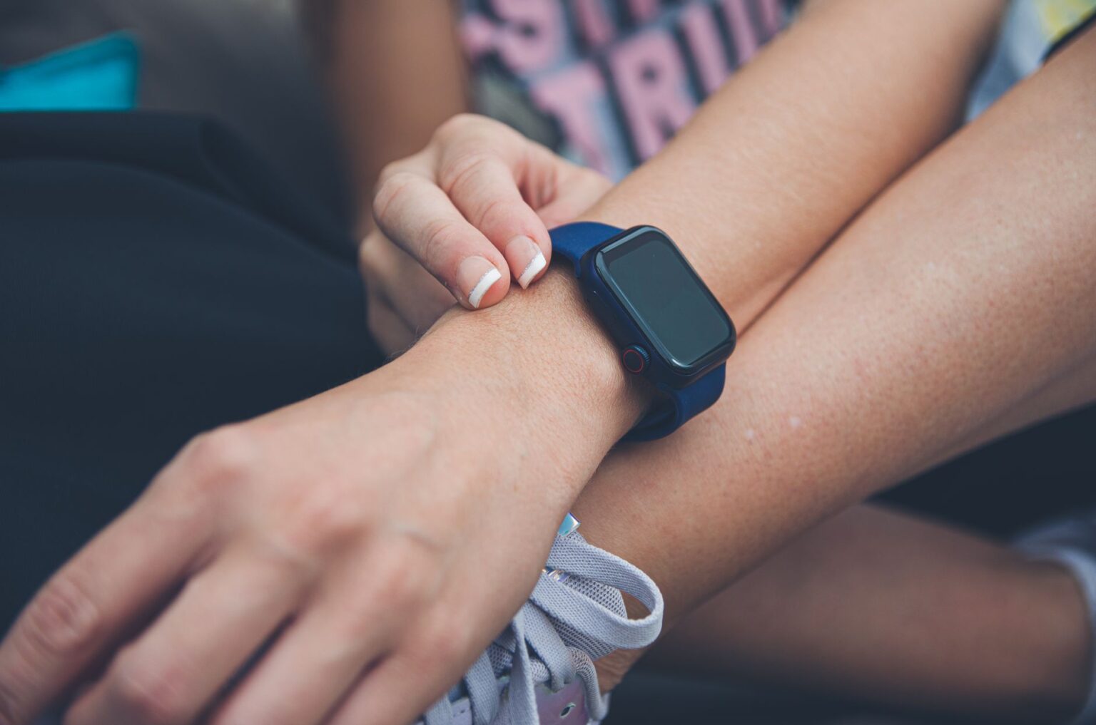 Kobieta sprawdza godzinę lub powiadomienia na Apple Watch z niebieskim paskiem założonym na nadgarstek